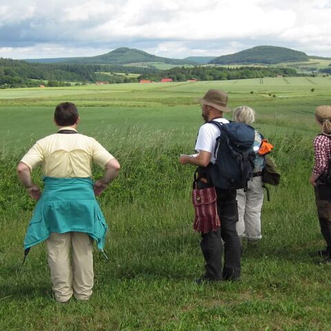 Eine Gruppe Wander:innen schaut über Felder hinweg zu Hügeln