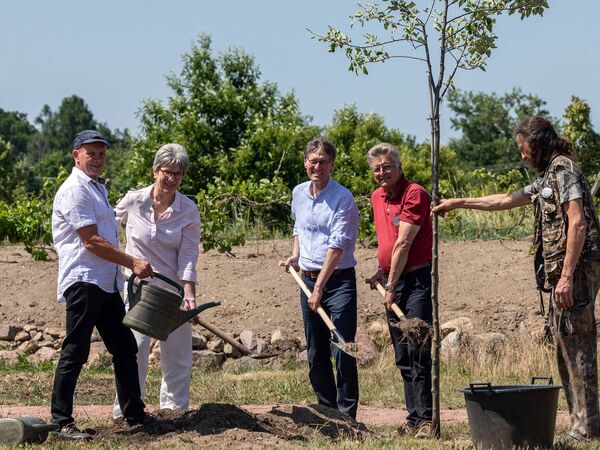Menschen Pflanzen einen Apfelbaum und halten Spaten und Gießkannen in der Hand.