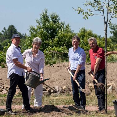 Menschen Pflanzen einen Apfelbaum und halten Spaten und Gießkannen in der Hand.