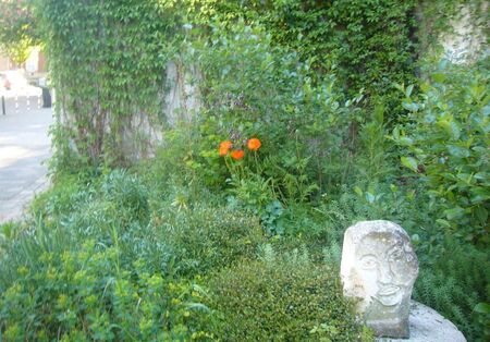 Ein Kopf aus Stein steht vor einer begrünten Wand 