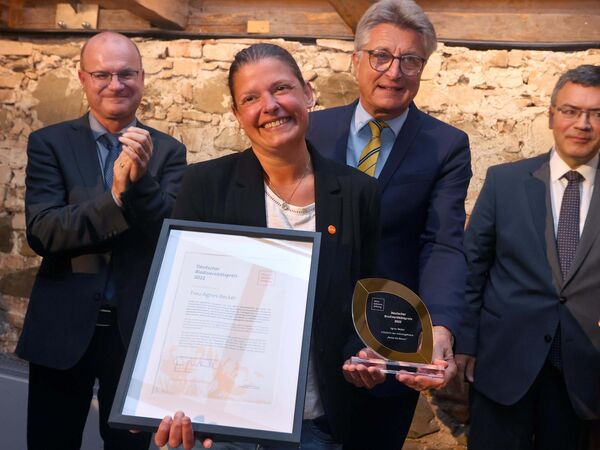 Biodiversitätspreis für Agnes Becker Preisträgerin Agnes Becker hält Ihre Urkunde und den Preis in den Händen und lächelt in die Kamera. Im Hintergrund stehen Fritz Brickwedde, Stiftungsratsvorsitzender und zwei weitere Herren.