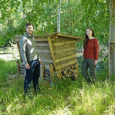 Eisvogel-Nisthilfe am Beuster Teich Junger Mann und Frau stehen von zwei Seiten neben einer Nisthilfe aus Holz