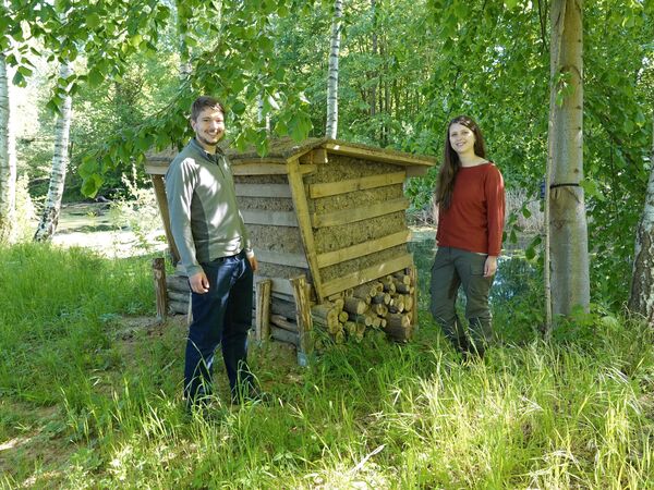 Junger Mann und Frau stehen von zwei Seiten neben einer Nisthilfe aus Holz