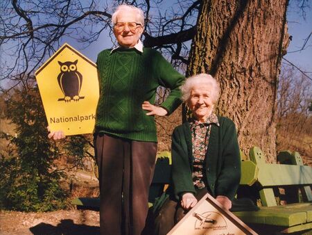 Ein älterer Herr und eine ältere Dame mit Holzschildern, auf denen eine Eule abgebildet ist